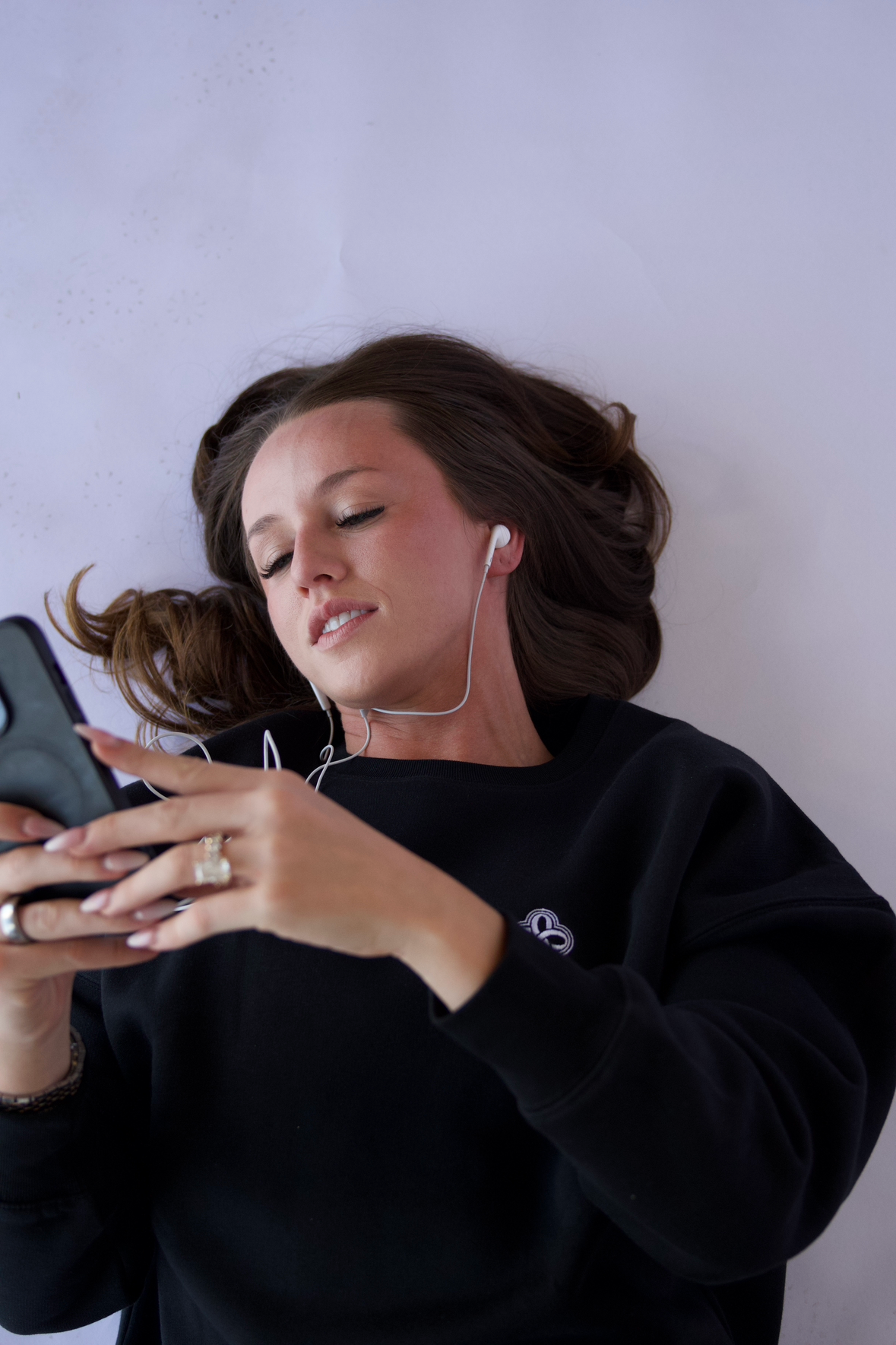 Person wearing a black sweatshirt with a logo, using a smartphone against a plain background