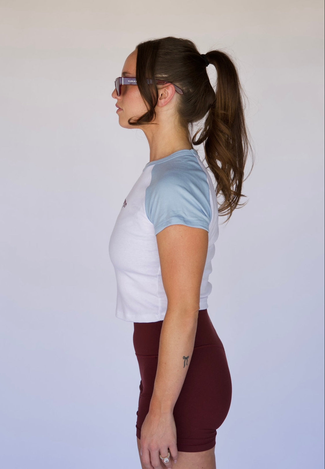 Woman wearing a white and light blue t-shirt with maroon shorts against a plain background