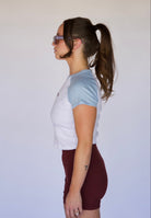 Woman wearing a white and light blue t-shirt with maroon shorts against a plain background