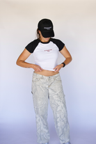 Person wearing a black and white t-shirt with text and light-colored pants against a white background